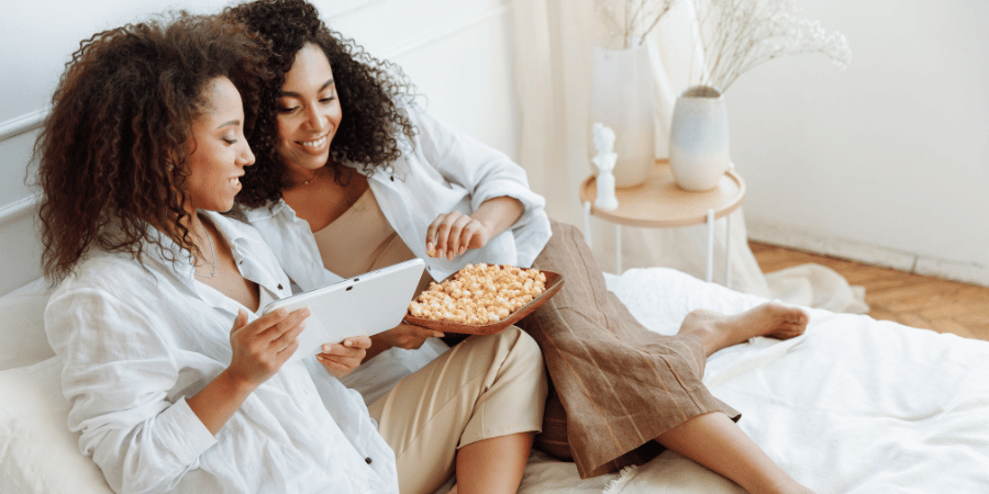 2 women eating pop corn on the bed